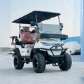 ocean cartz dramatic, low-angle front view of a white lifted golf cart with a black roof and black accents. This off-road electric vehicle features huge, aggressive all-terrain tires on black custom wheels, a heavy-duty brush guard, and a front cargo basket mounted above the hood. The four-seater utility cart has dark red or brown leather seats and is pictured outdoors in an open area with a bright sky.