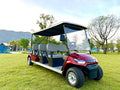 Red electric golf cart with multiple seats on a grassy area with trees and mountains in the background.