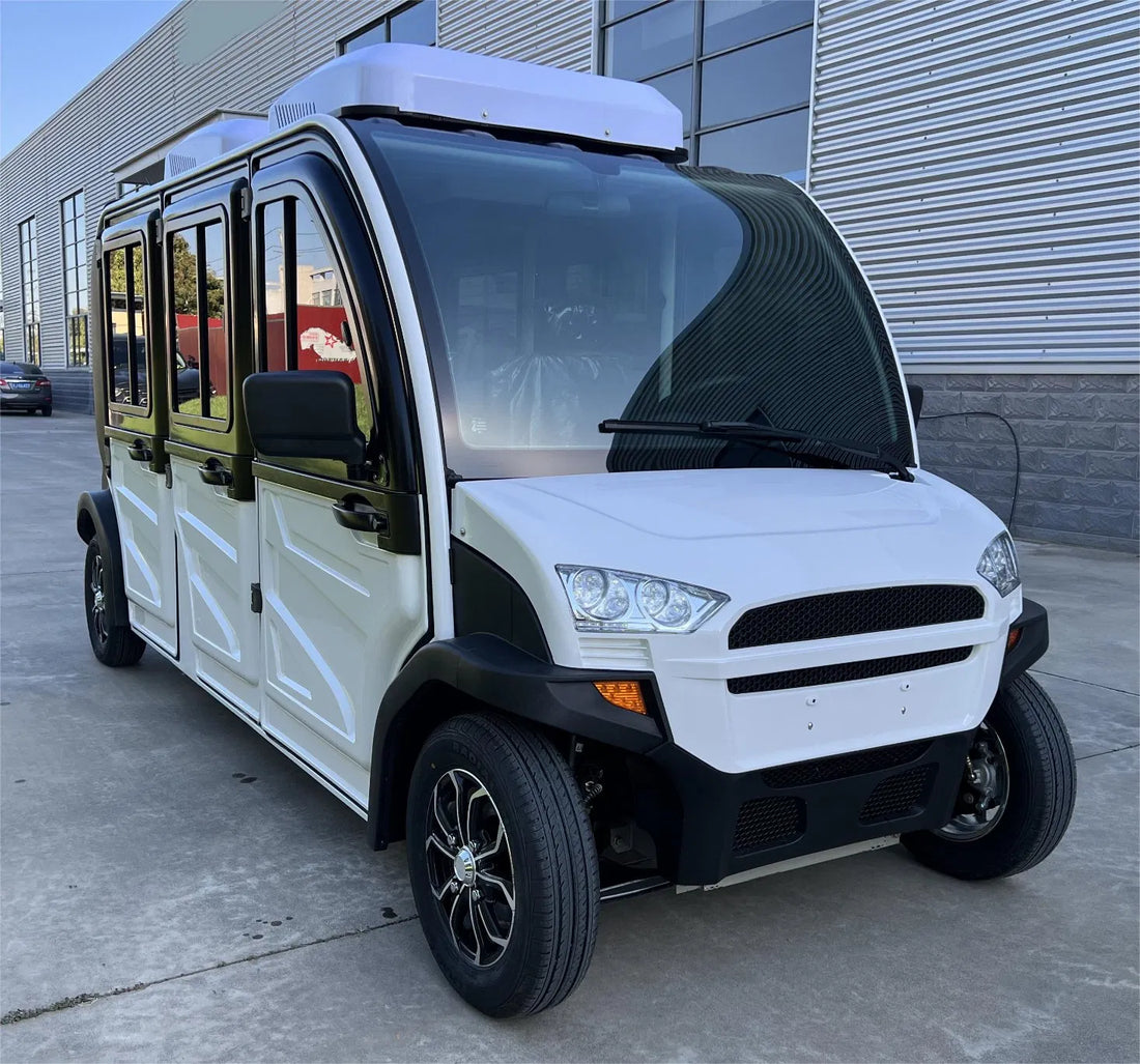 White electric vehicle with open doors on a concrete surface, surrounded by greenery.