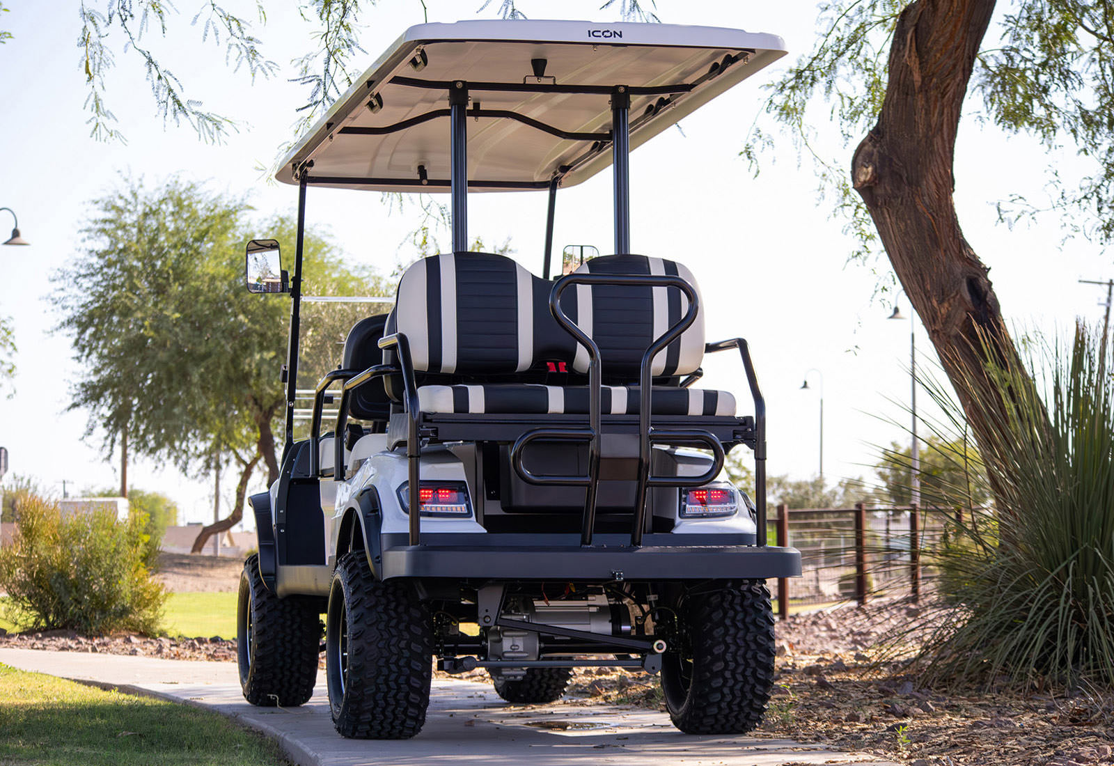 Golf cart with open top on a paved path surrounded by trees and shrubs