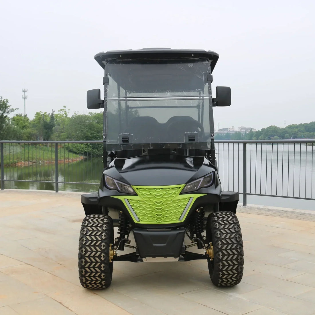 Black and green golf cart on a wooden deck with a lake and trees in the background