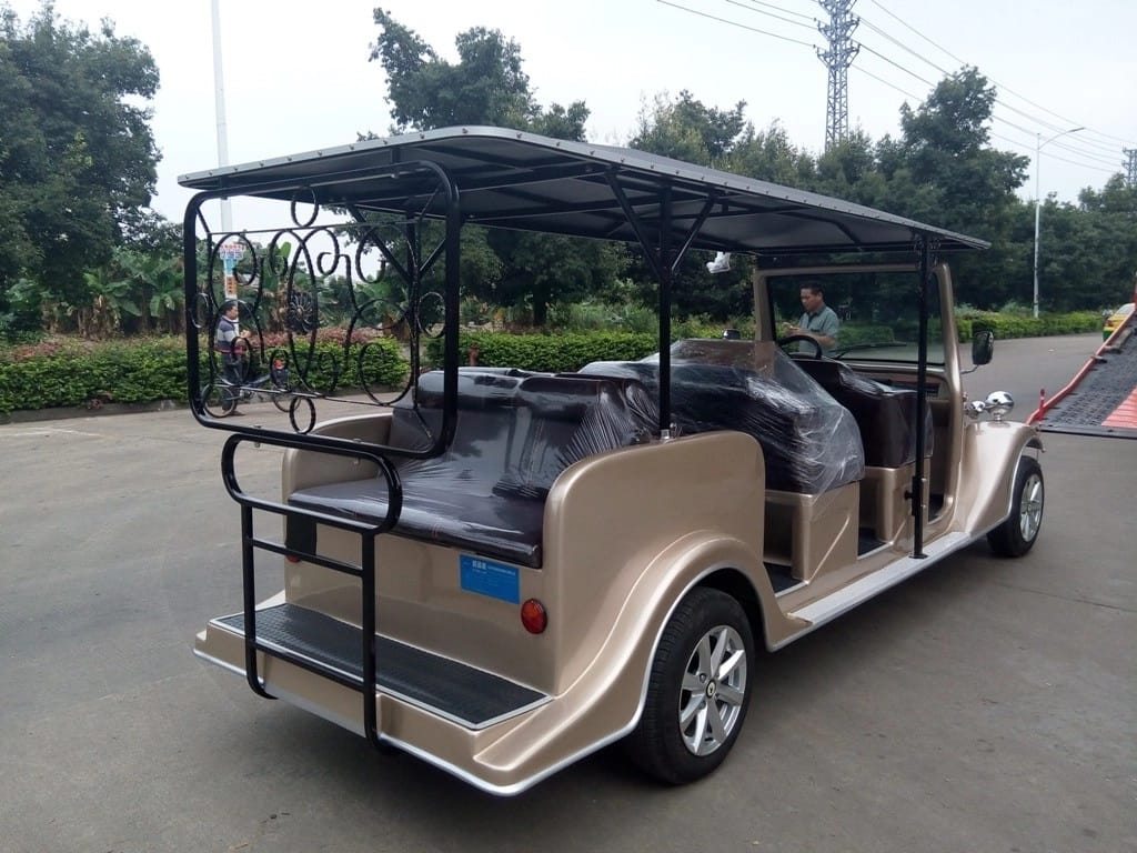 Vintage-style vehicle parked in an industrial area with buildings and trees in the background.