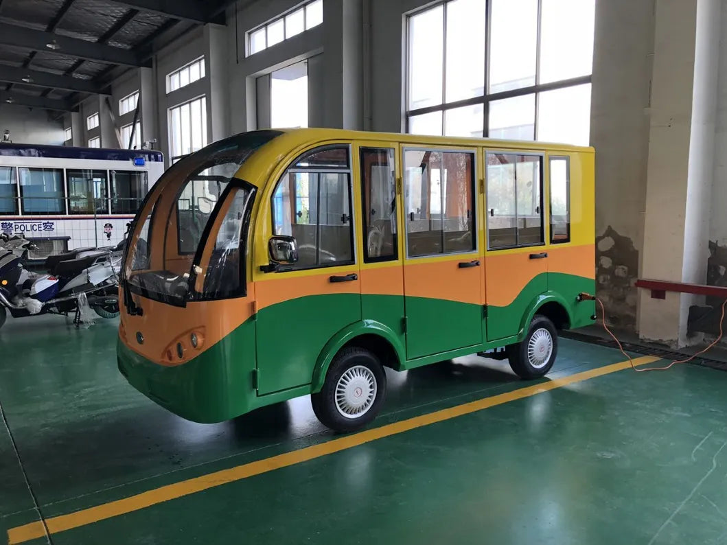 Small green and orange vehicle in a large indoor setting with high ceilings and large windows.