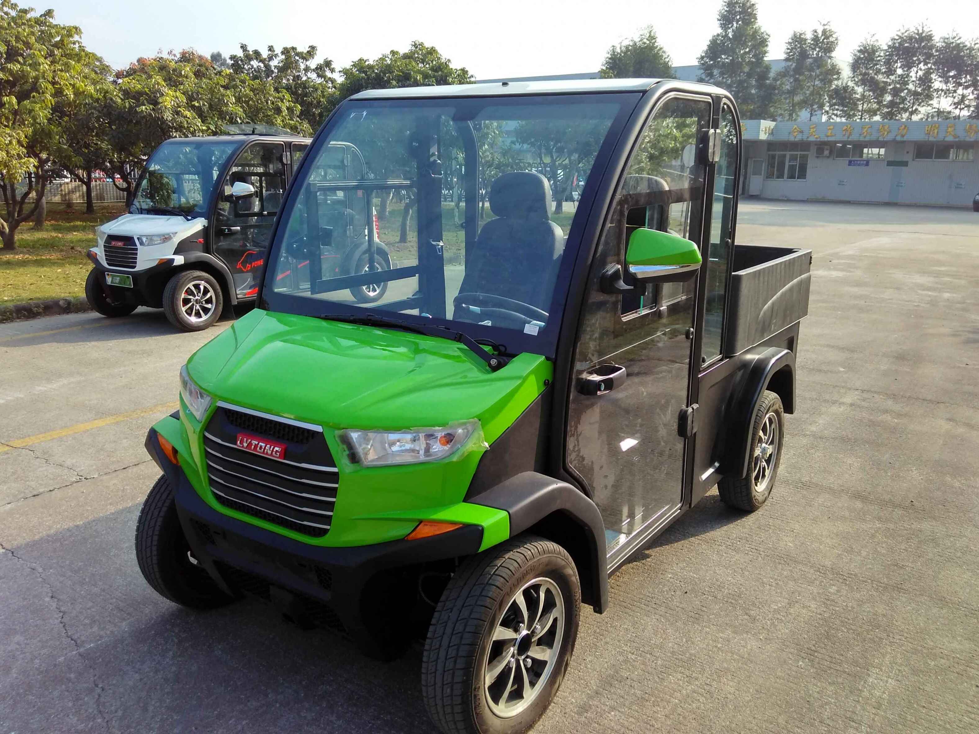 Green and black electric vehicle with a small cargo bed on a paved area.