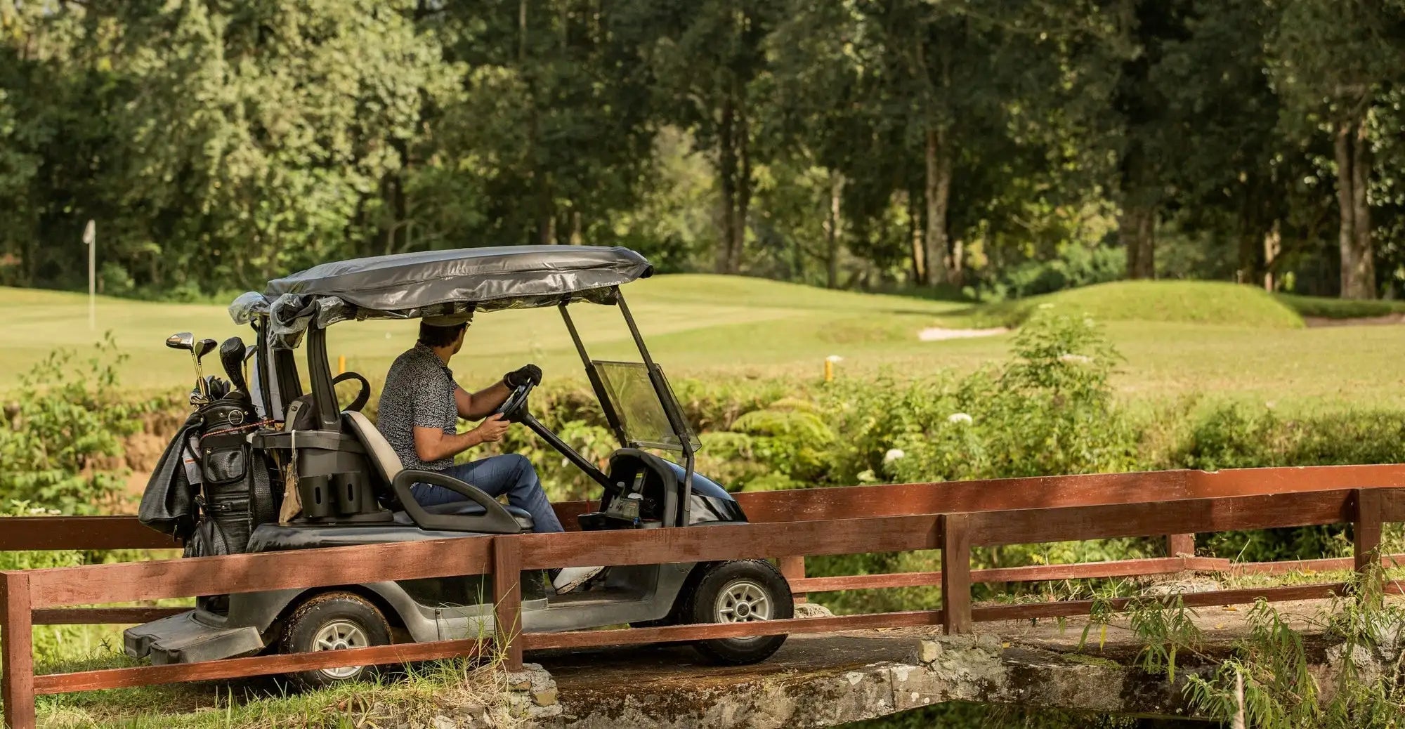 Black and gray golf cart with a canopy, carrying clubs on its side.