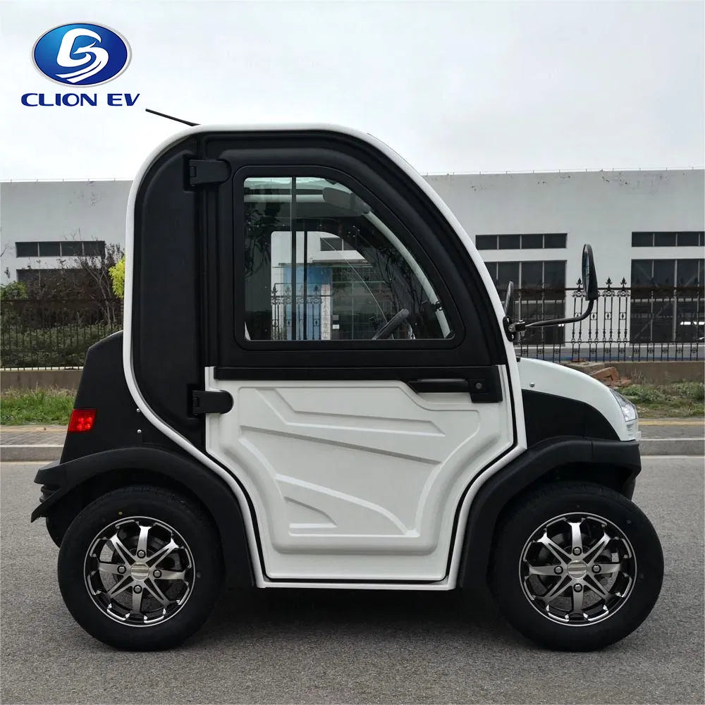 ocean cartz side profile view of a white and black two-seater electric vehicle with a fully enclosed cab, parked on an asphalt road. This compact low-speed electric car or NEV features a large driver's door with a pronounced white panel design, black fender flares, and a small rear window. It is equipped with custom black and chrome alloy wheels, emphasizing its all-weather neighborhood electric car design.