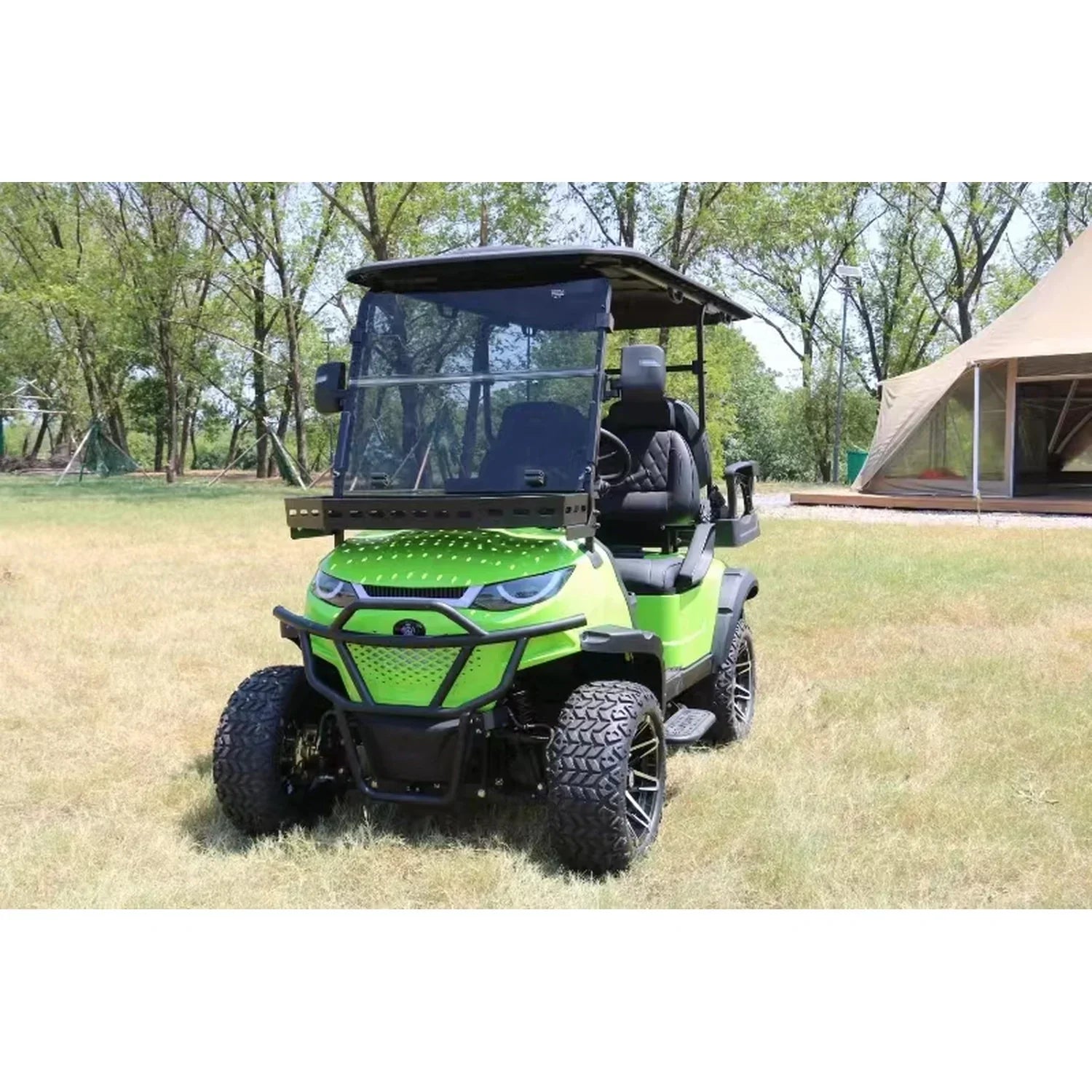 A bright green, customized off-road golf cart with large all-terrain tires, a black roof, and a rugged front bumper, parked on a grassy field in an outdoor setting.