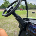 Steering wheel and dashboard of a vehicle with a grassy field and trees in the background