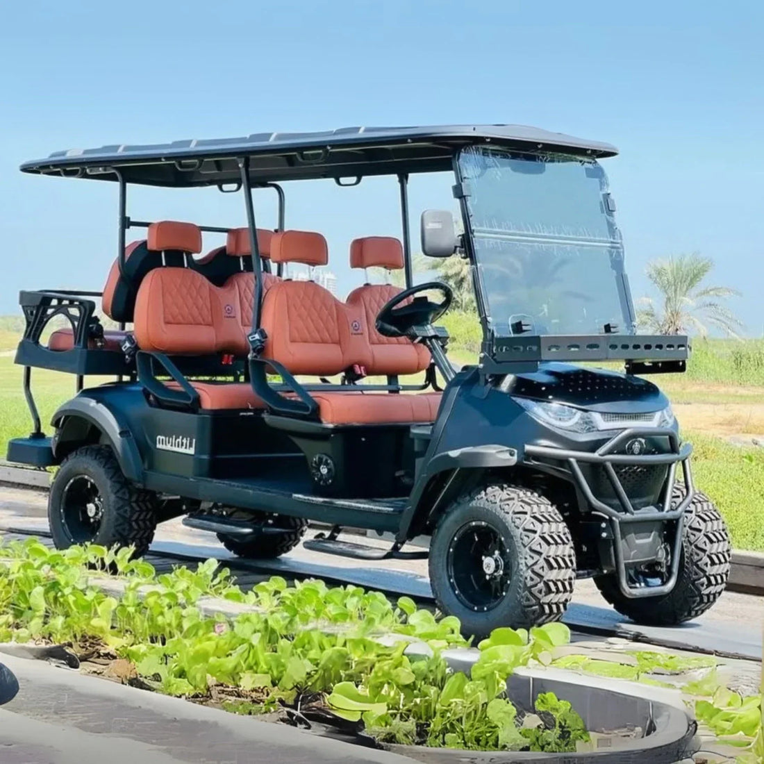 Golf cart with red seats on a platform, with greenery and clear sky in the background