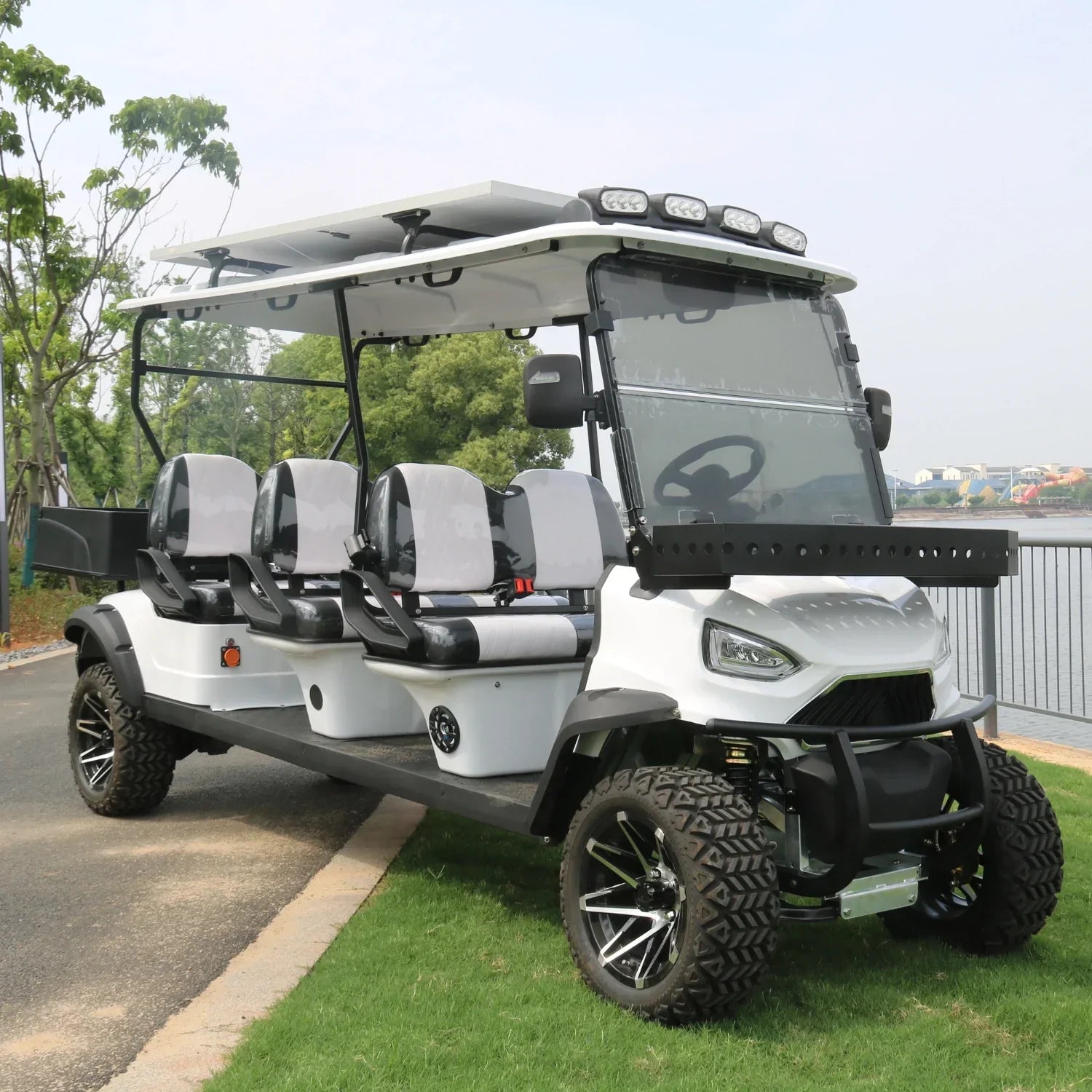 White golf cart with six seats on a grassy area near a body of water.