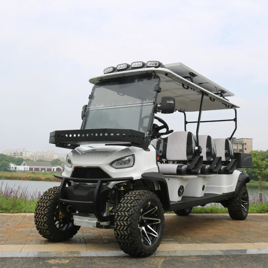 White golf cart with black accents parked by a lake with greenery and buildings in the background.