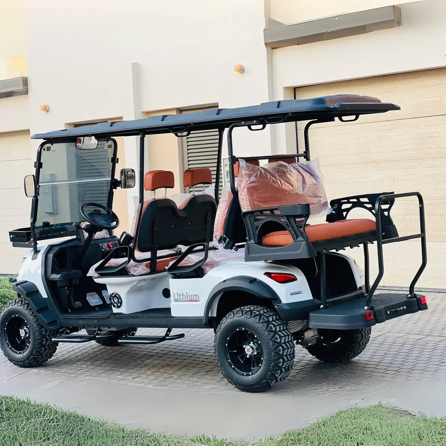 White golf cart with black roof and orange seats parked on a driveway.