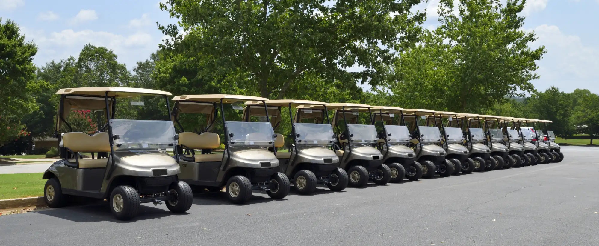 A row of beige and gray golf carts with tan seats, lined up neatly on a paved surface.